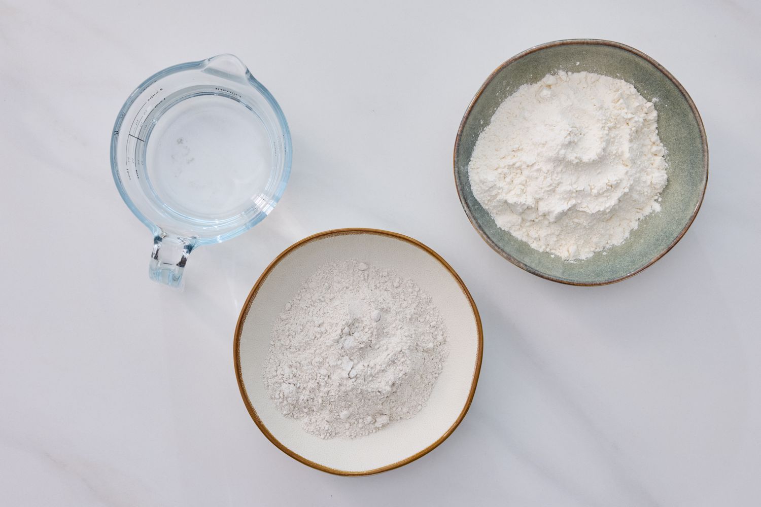 Three bowls containing water flour and flour with a distinct appearance ingredients for sourdough starter