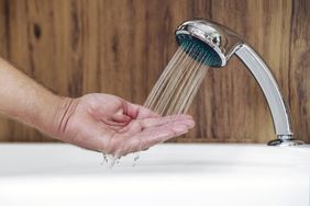 A man uses hand to measure the water temperature from a water heater before taking a shower