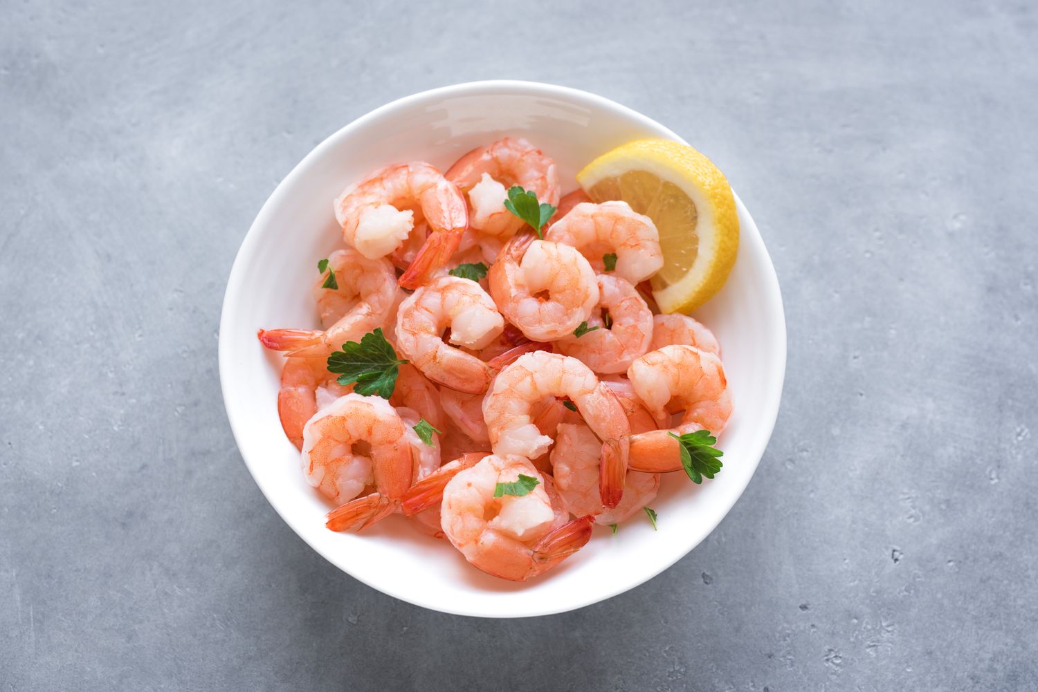 A bowl of cooked shrimp garnished with parsley and a lemon wedge