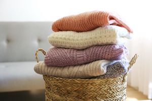 A bunch of stacked knitted pastel color sweaters with different knitting patterns perfectly folded in wicker basket on table, living room background.