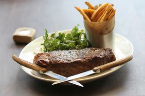 steak with tallow fries and salad on white plate with 2 knives