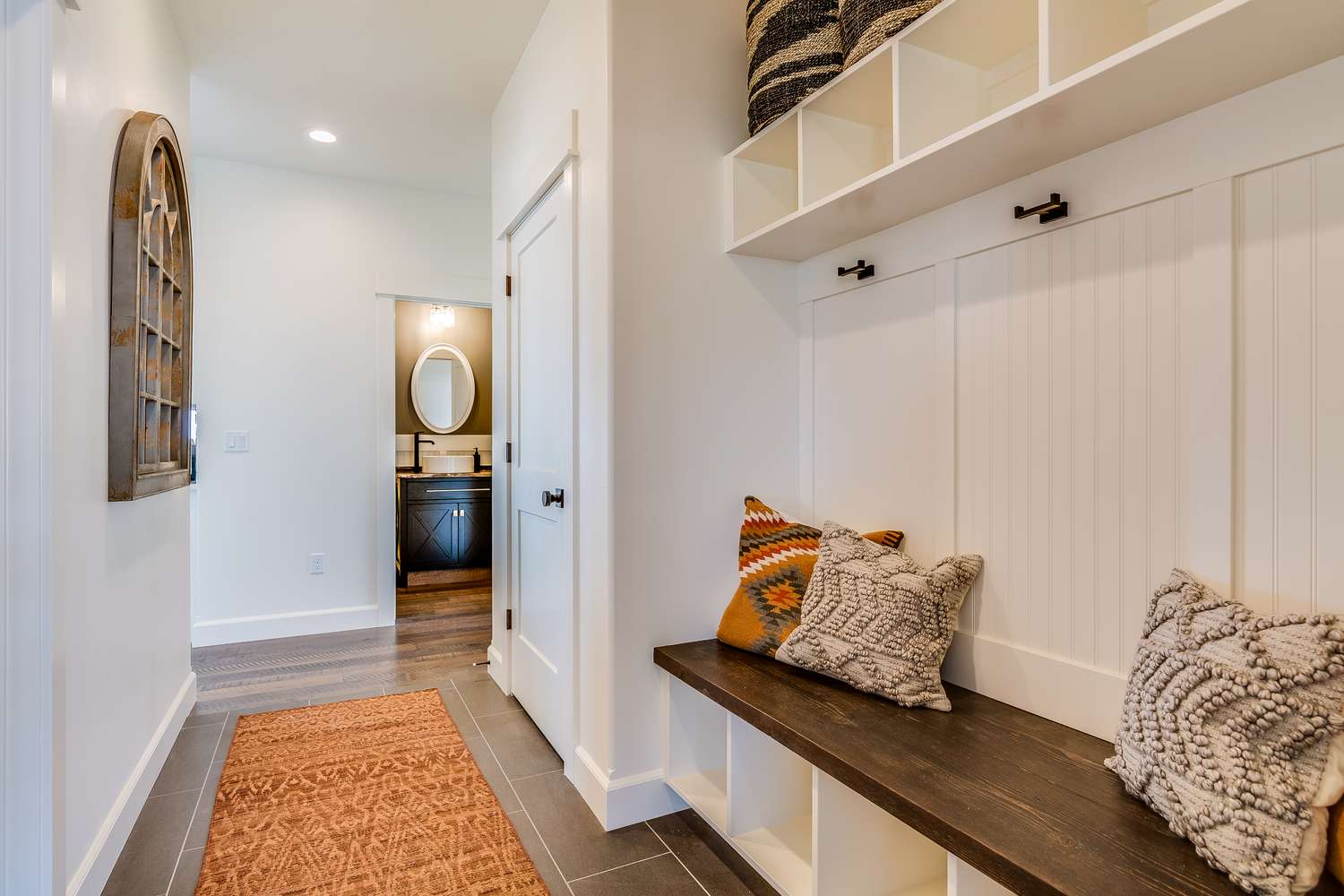 Entryway with builtin bench seating decorative pillows and a view into a bathroom with an oval mirror