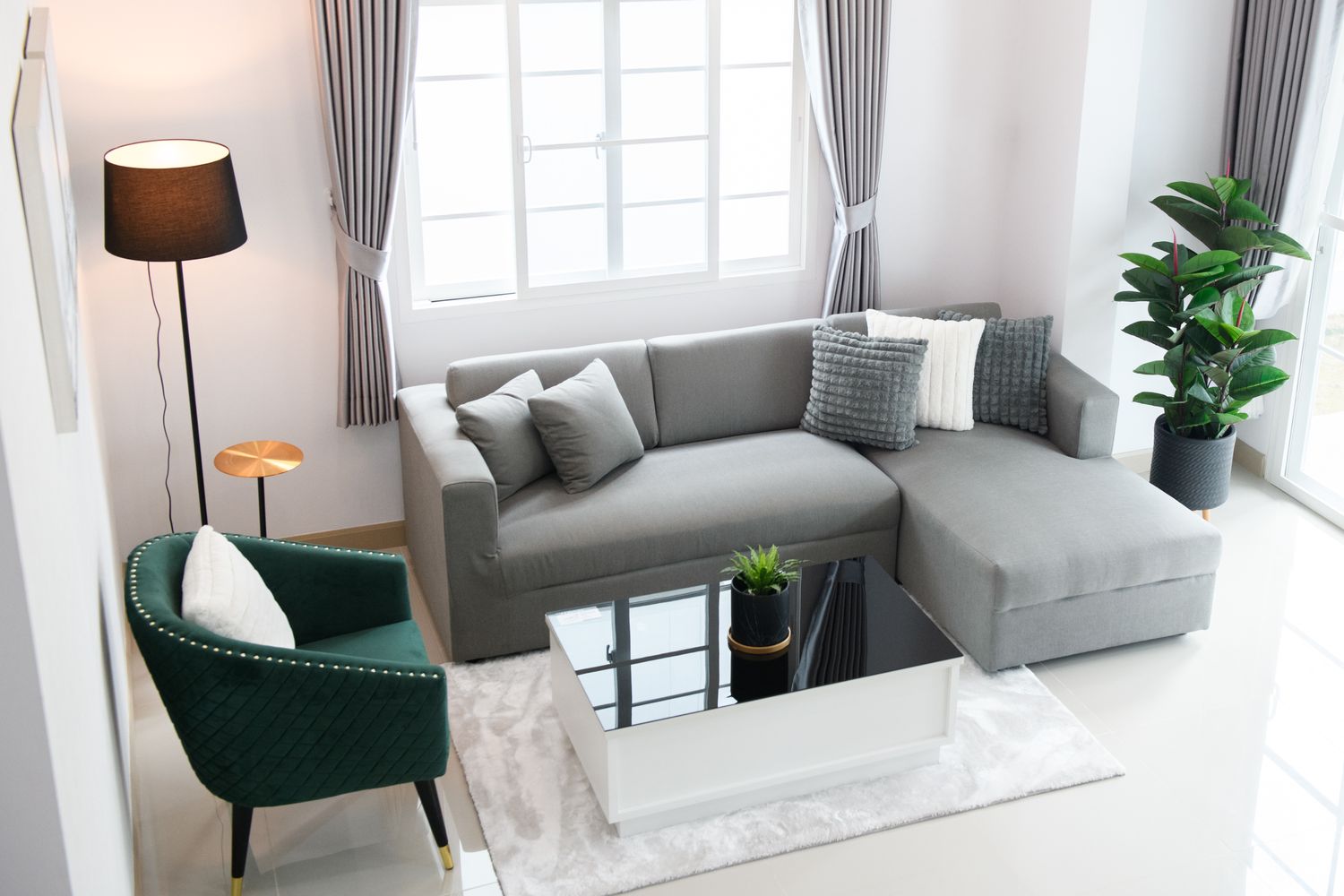 Modern living room with a gray sofa green armchair coffee table and indoor plants near a window with curtains