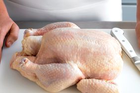 raw whole chicken on cutting board with knife and person in white