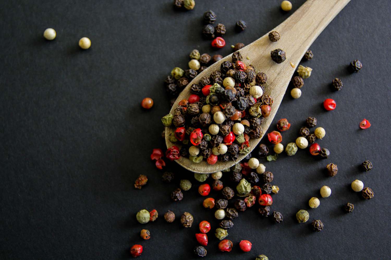Mixed peppercorns including red, green, black, and white dried peppercorns in a spoon