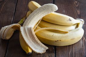 Several bananas, one partially peeled, on a wood surface