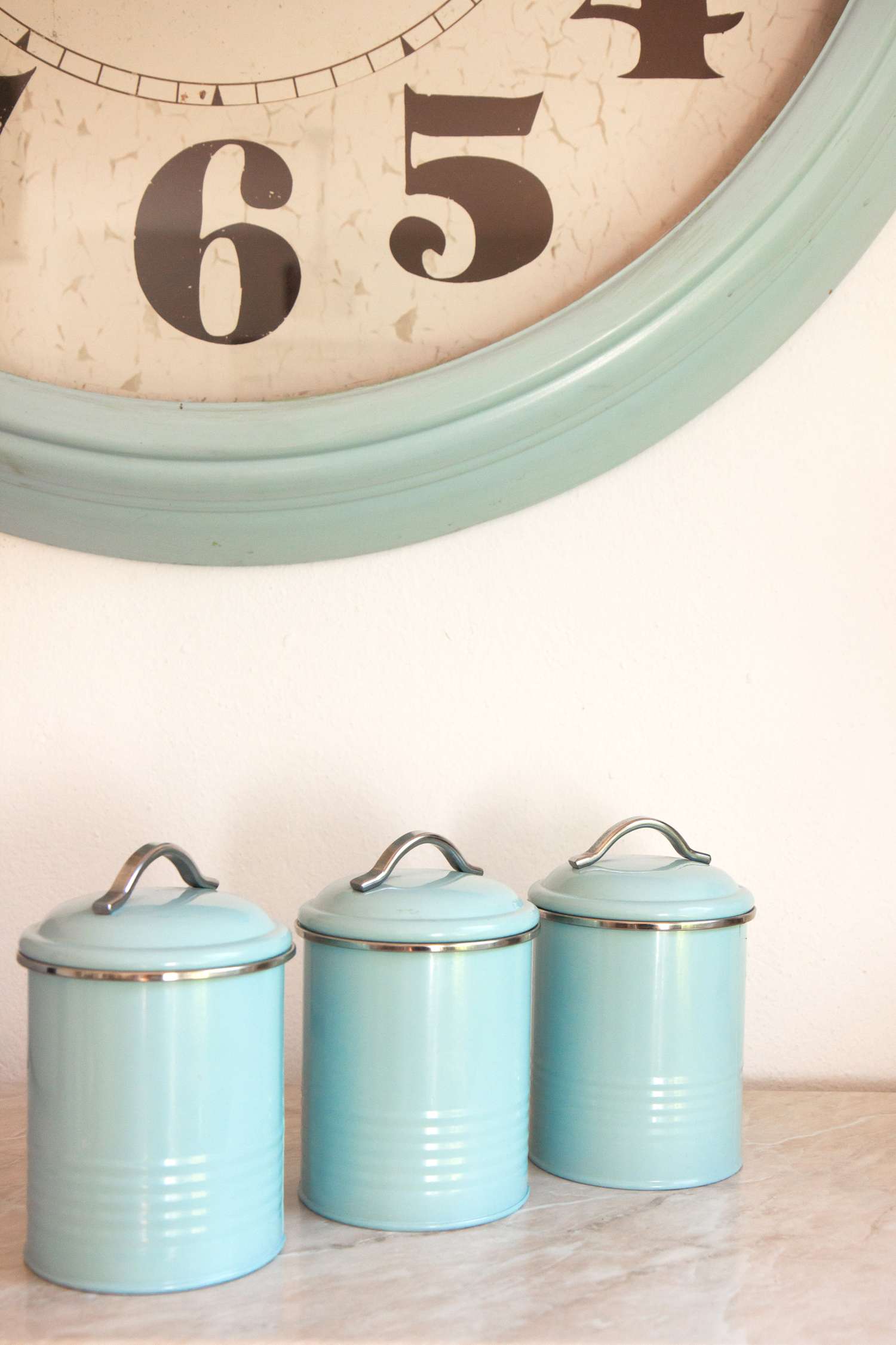 A large clock and three kitchen canisters on a counter