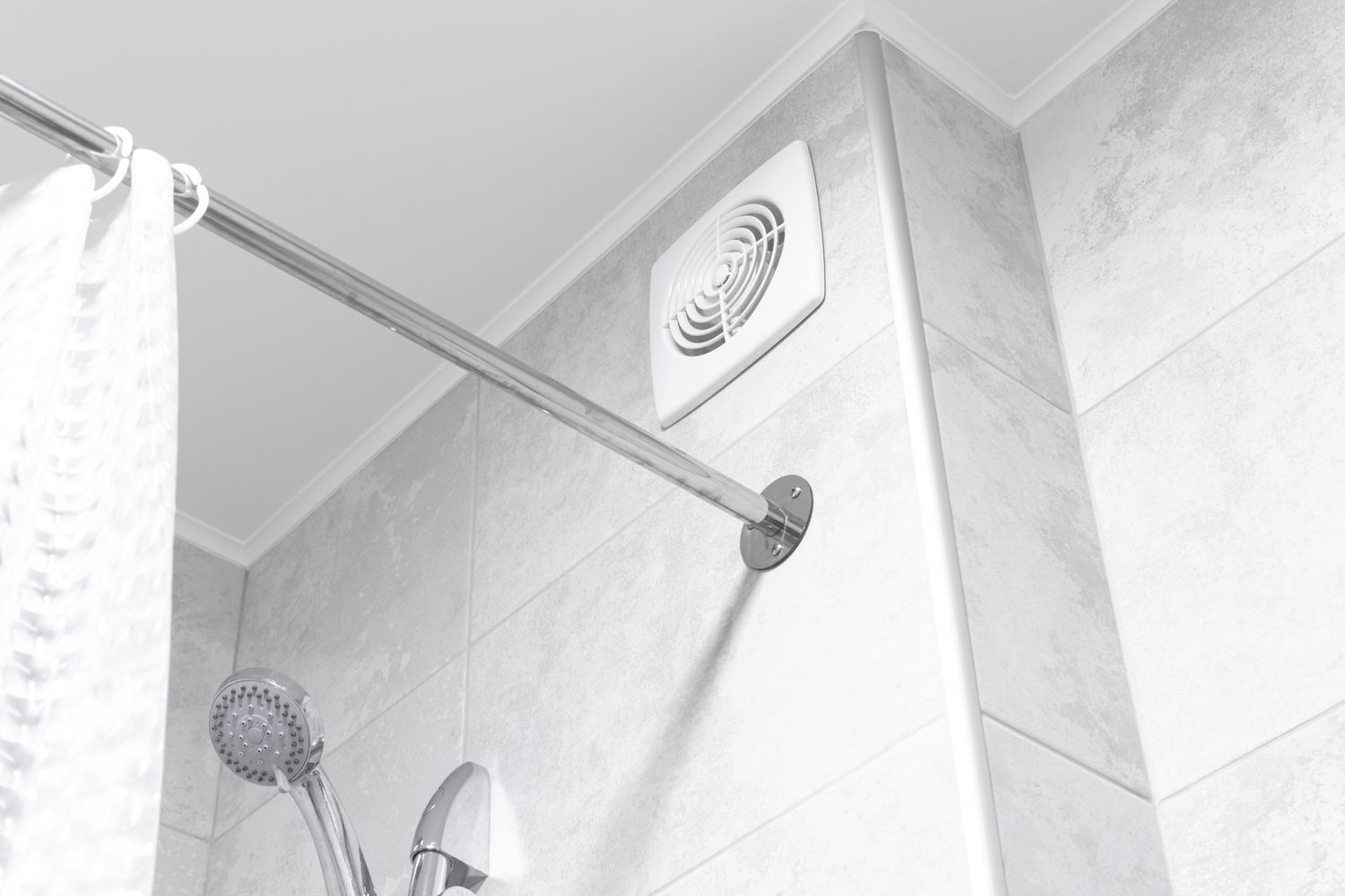 A bathroom scene showing a shower rod a shower head and a ceiling vent in a tiled setting