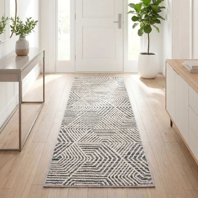 A hallway with a patterned runner rug a console table with decor a plant and natural light from a door and windows