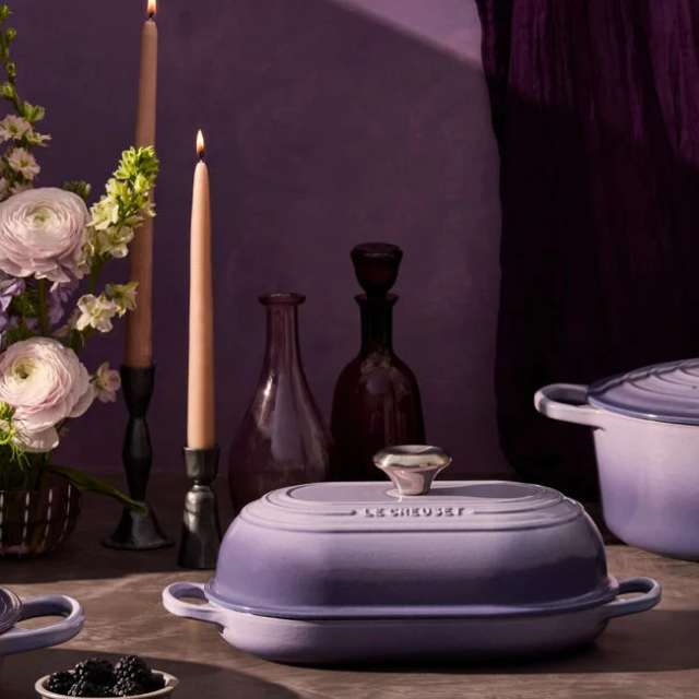 Set of Le Creuset cookware with flowers and candles in the background on a table