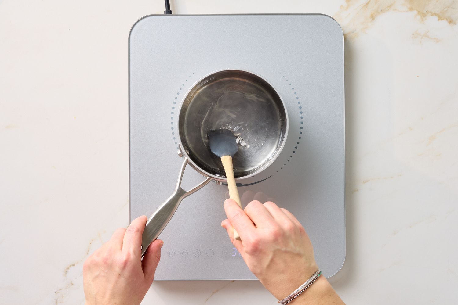 Hands stirring a liquid in a pot on a stovetop using a spoon and spatula
