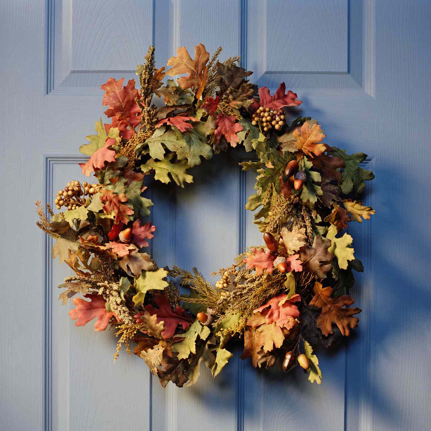 A fallthemed wreath with leaves and berries hung on a door