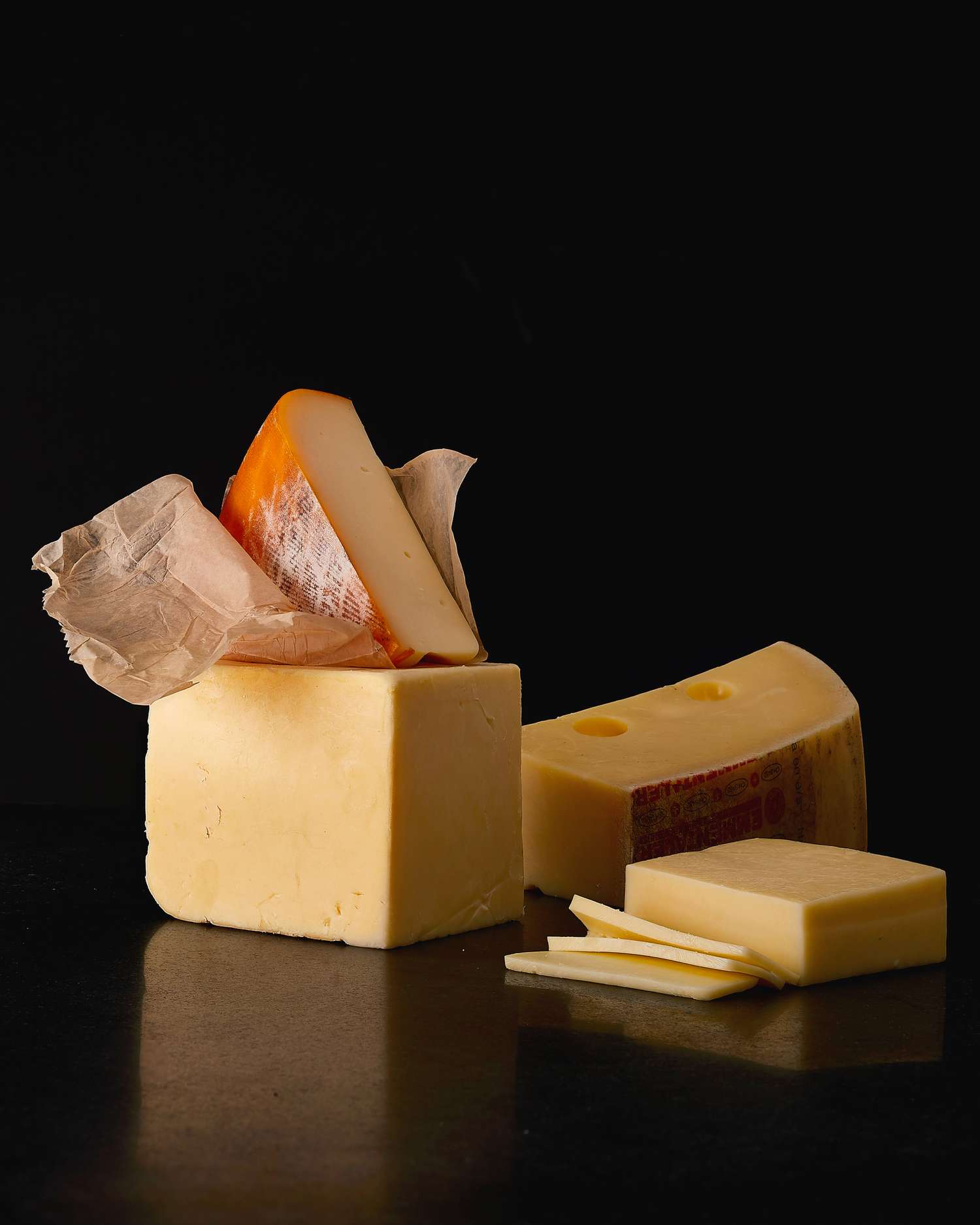 pieces of semi hard cheese, including cheddar and Emmental, on black surface