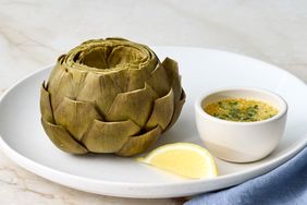 Steamed artichoke served on a plate with tarragon butter and a lemon wedge