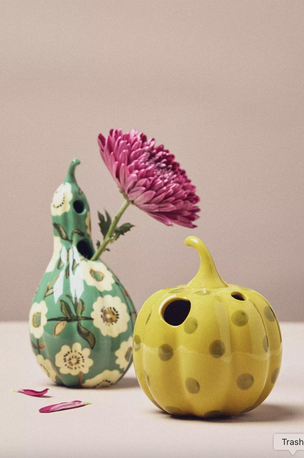 Decorative ceramic vases one shaped like a gourd with a floral pattern and the other resembling a pumpkin with polka dots both holding a pink flower