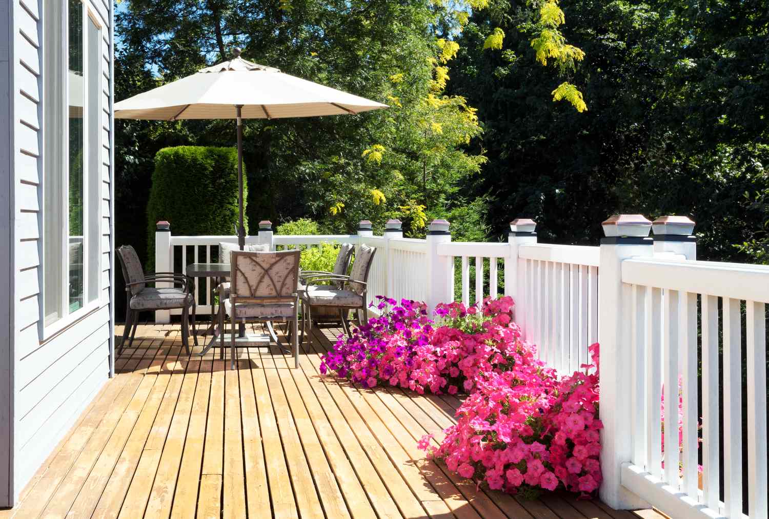 A wooden deck with patio furniture umbrella and pink flowers along the railing