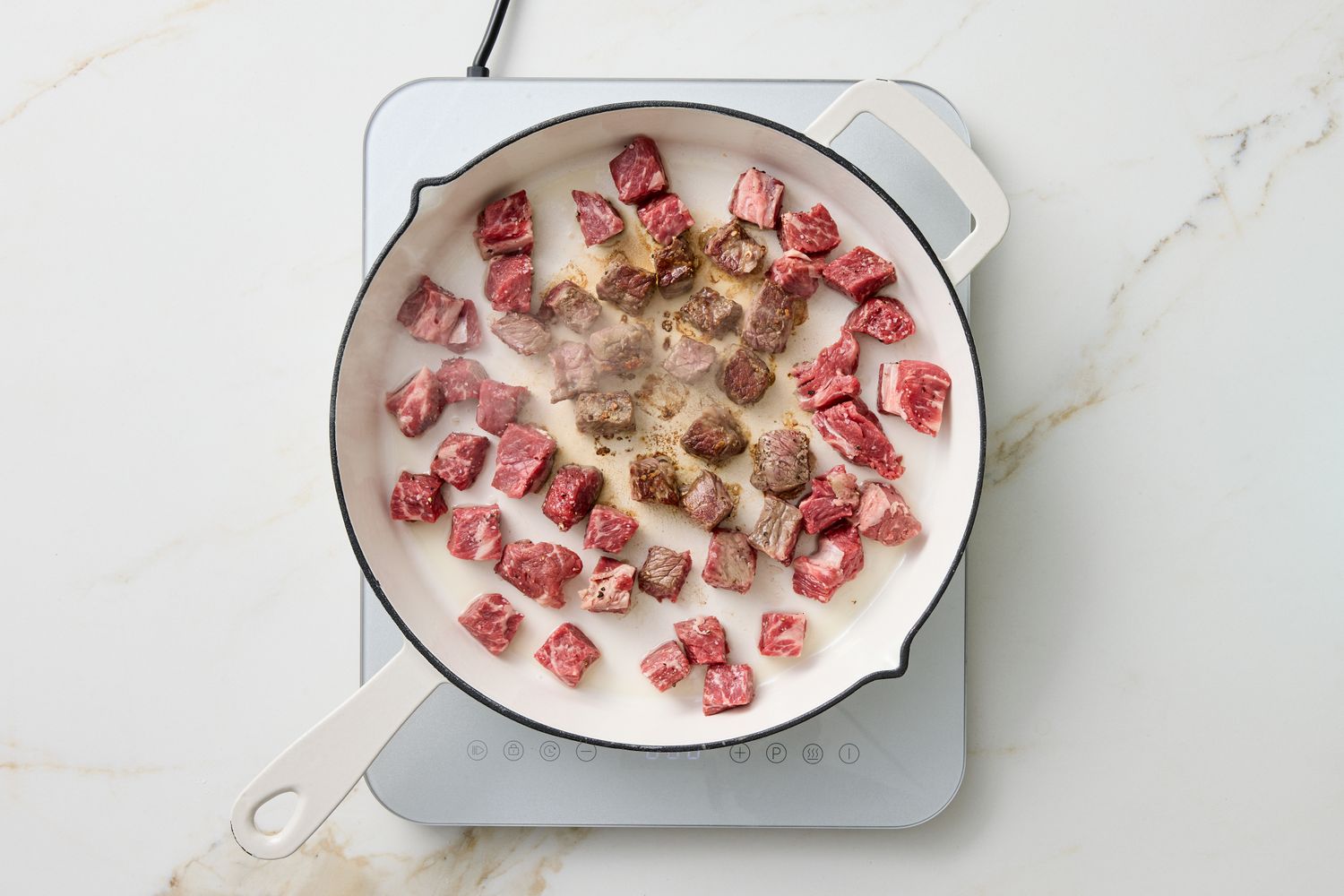 Cubed meat being cooked in a pan on an induction stove