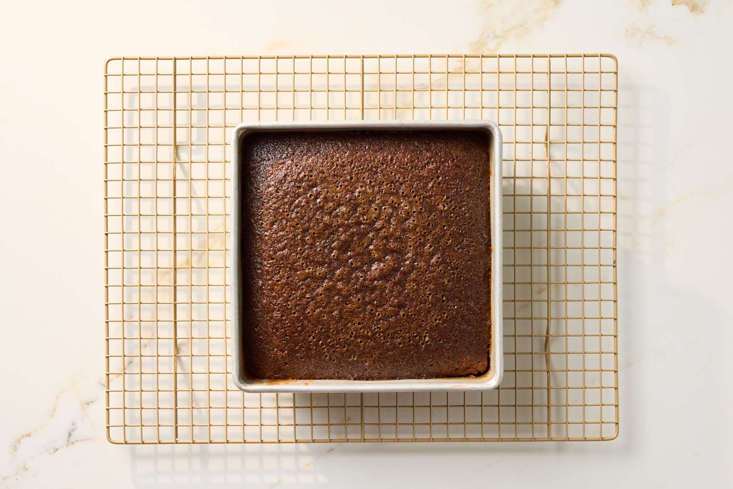 A square chocolate cake in a baking dish on a cooling rack
