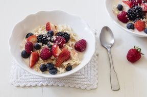 A bowl of oatmeal topped with berries and coconut with a spoon nearby on a textured mat