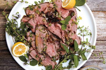sliced lamb on a plate with herbs and lemon
