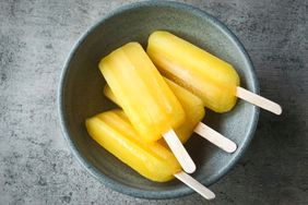 A bowl containing four yellow popsicles on a gray surface