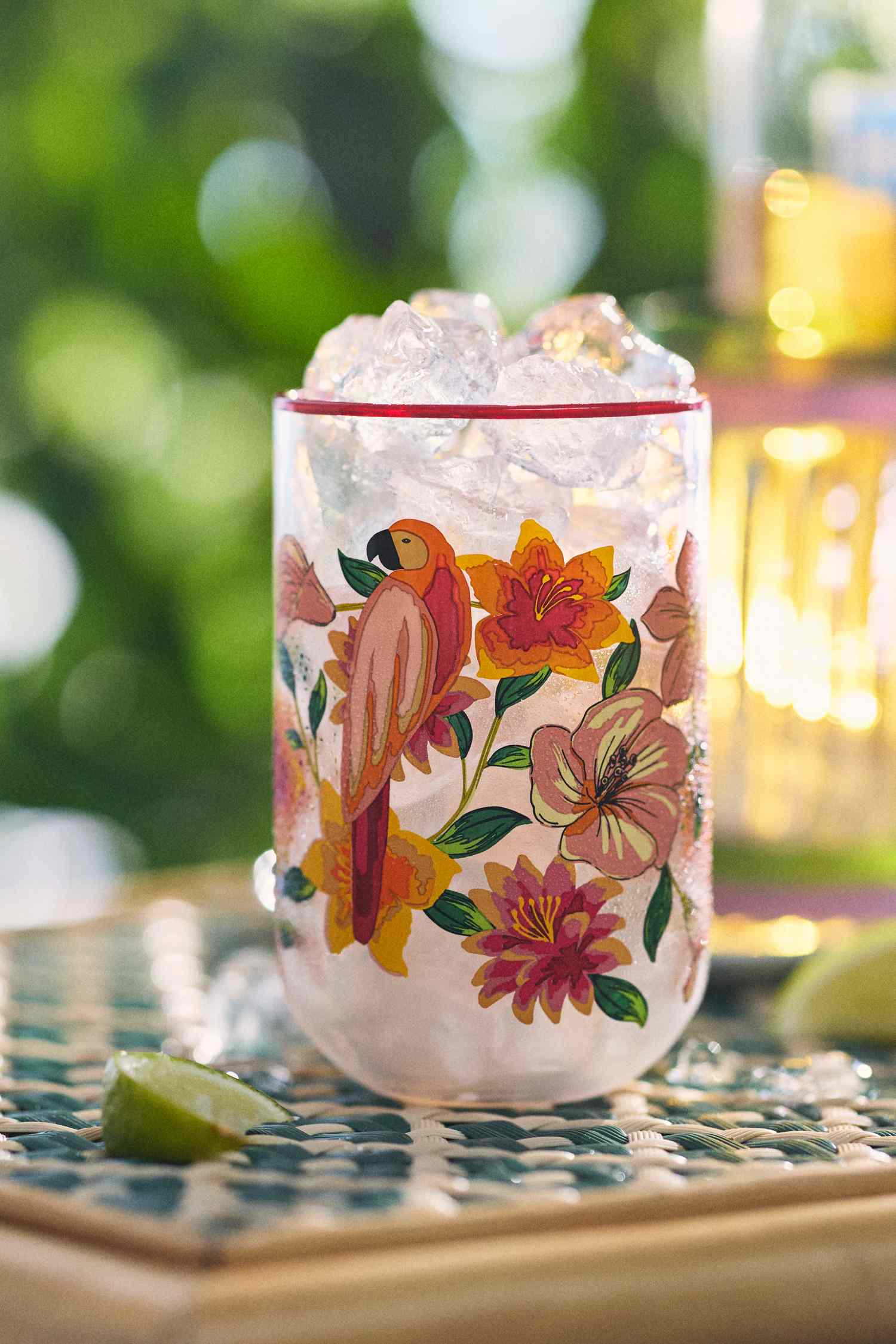 A decorative glass with floral and bird motifs on a patterned surface filled with ice with a blurred natural background