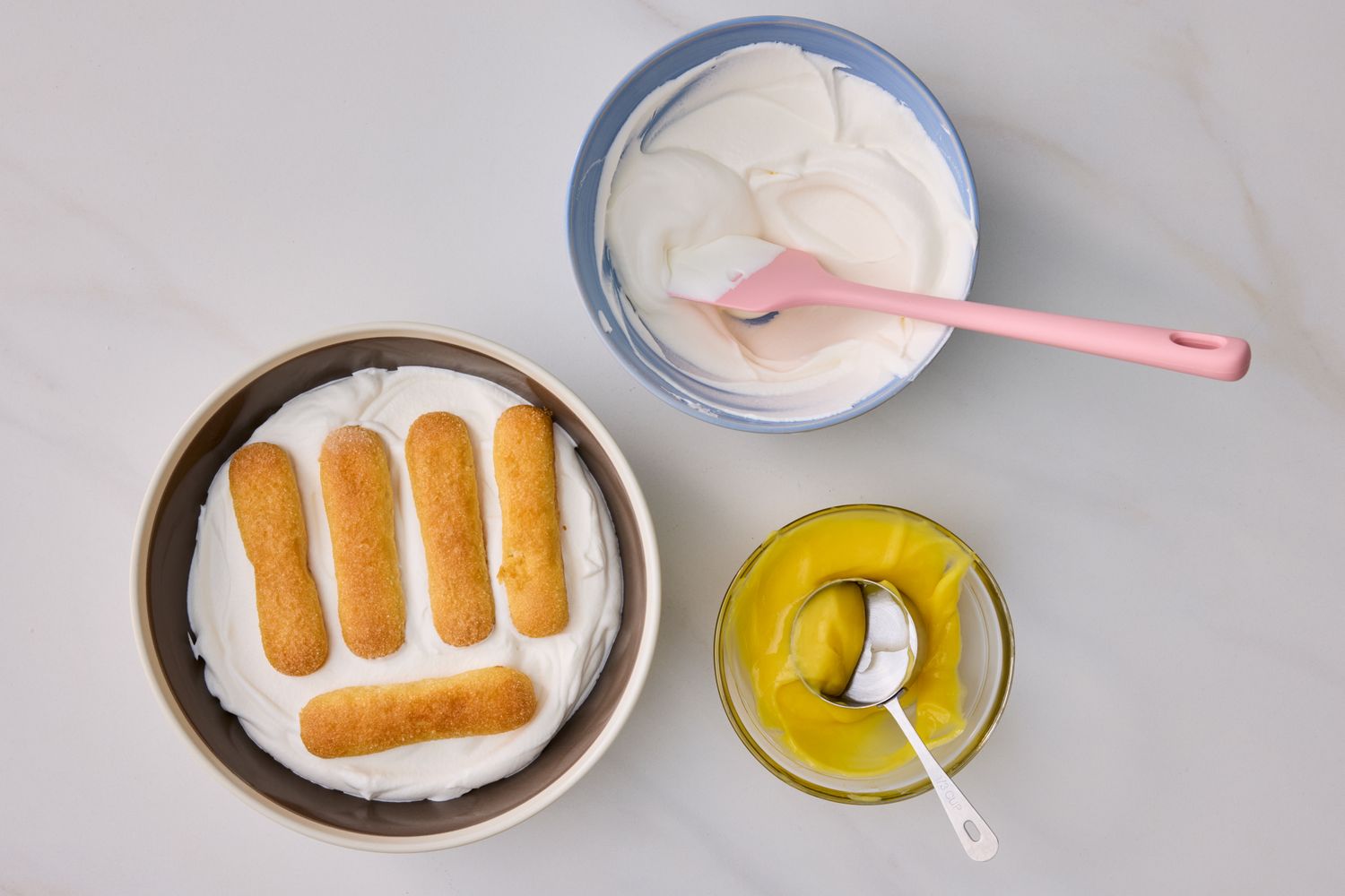 Ingredients for a lemon trifle with ladyfingers cream mixture and lemon curd in bowls with utensils