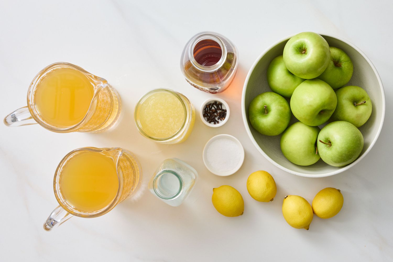 Ingredients including apples lemons and liquids in pitchers arranged on a surface