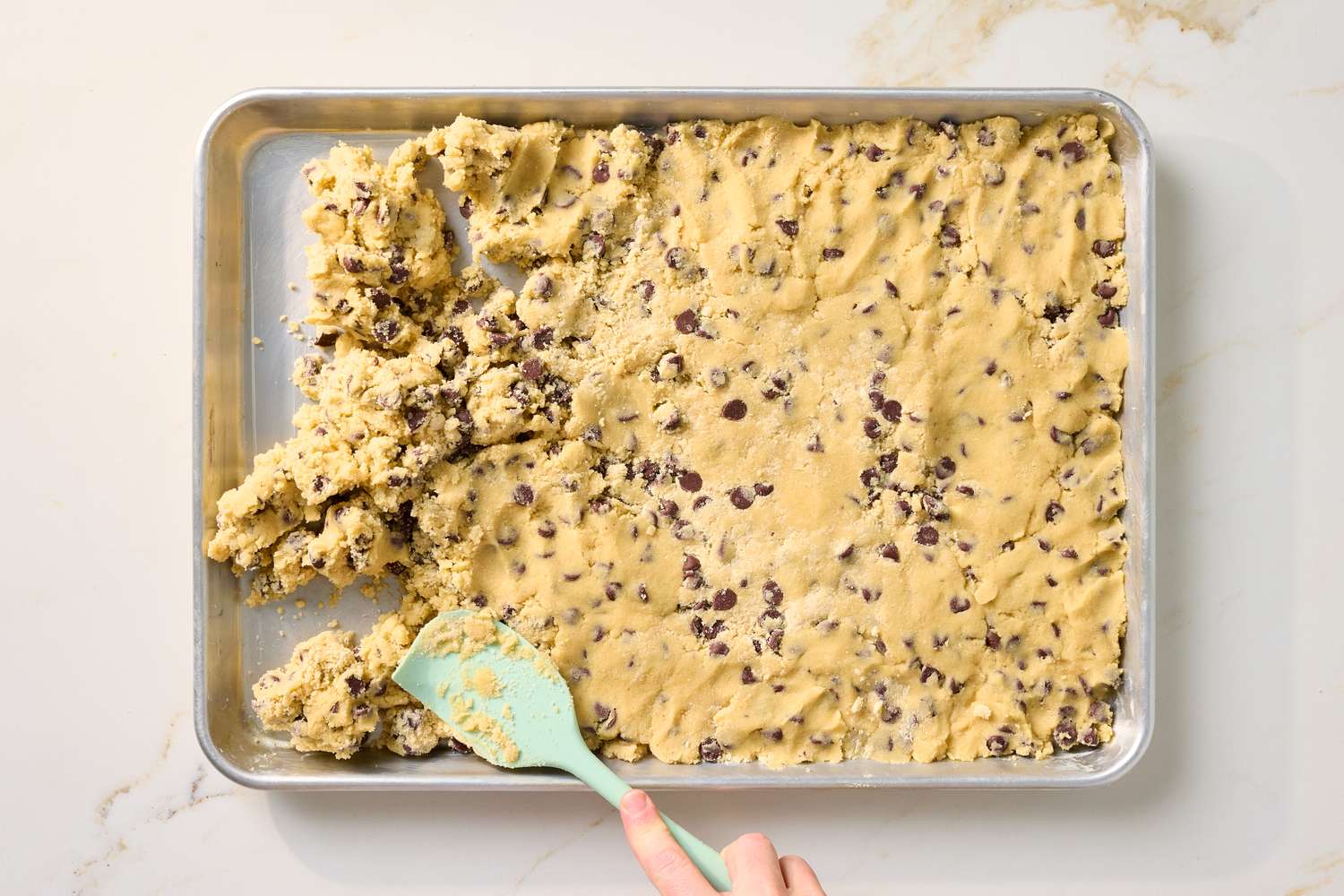 A baking sheet with chocolate chip cookie dough being spread out
