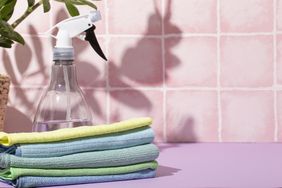 Cleaning spray bottle and folded microfiber cloths on a surface in front of pink tiles