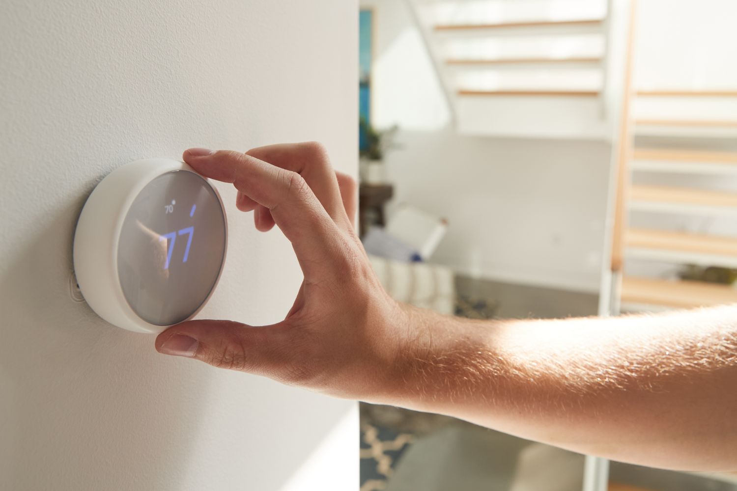 Hand adjusting a digital thermostat on a wall part of a smart home setup