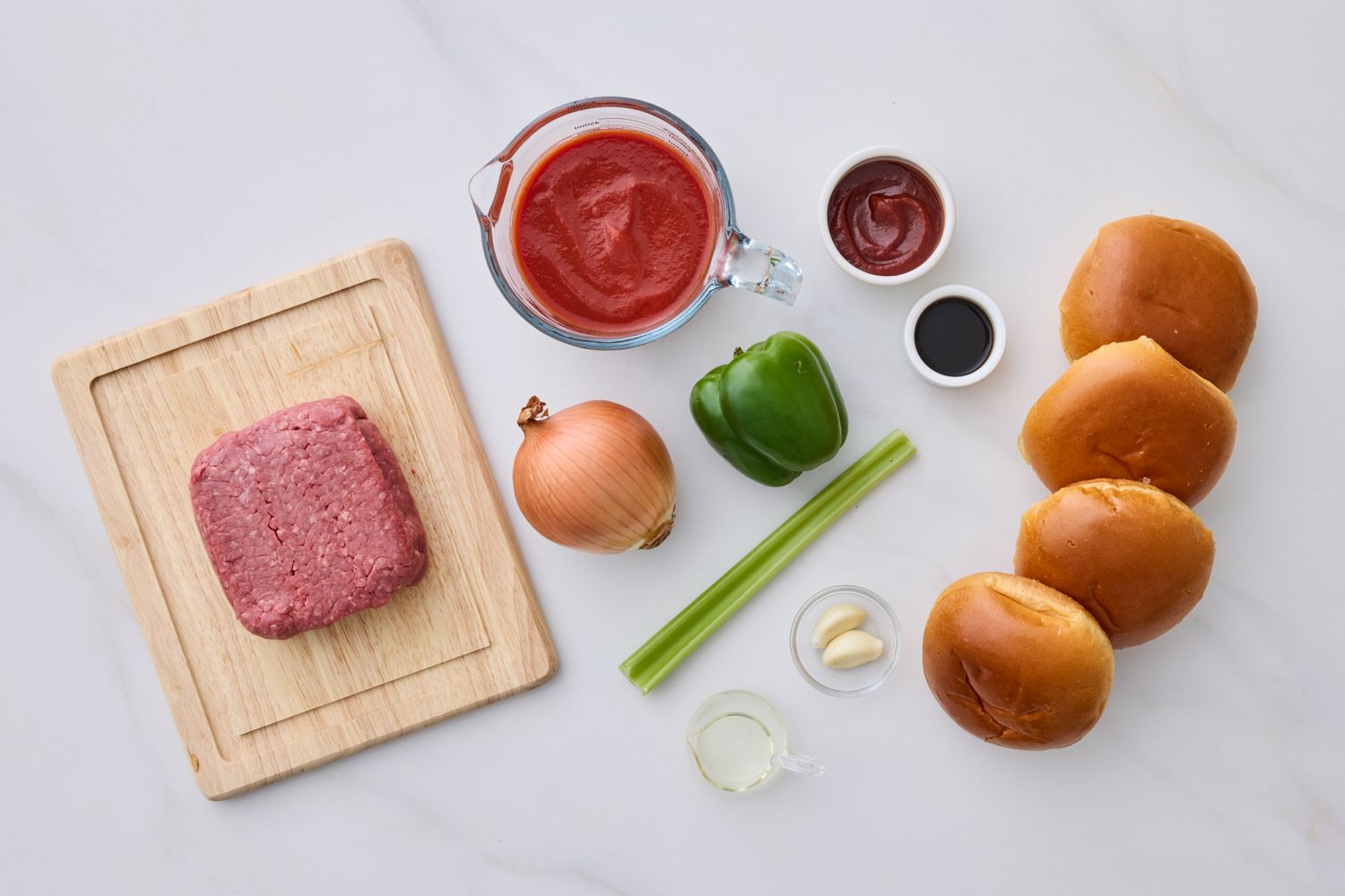 Ingredients for a sloppy joe recipe arranged on a surface including ground meat onion green pepper celery sauces buns and seasonings