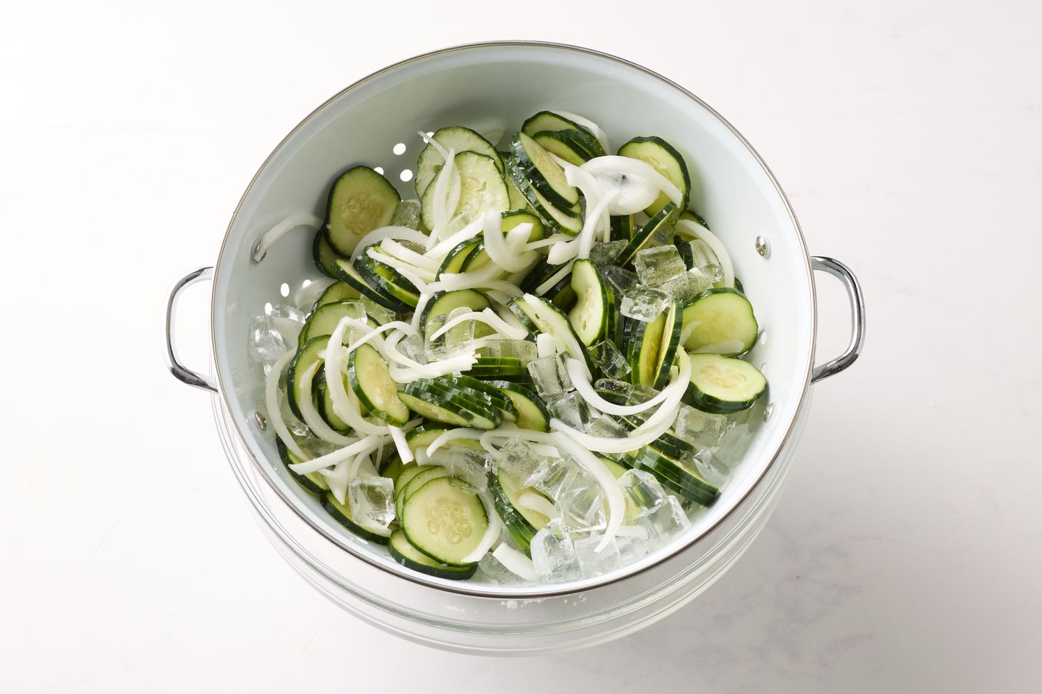 Sliced cucumbers and onions in a colander with ice cubes