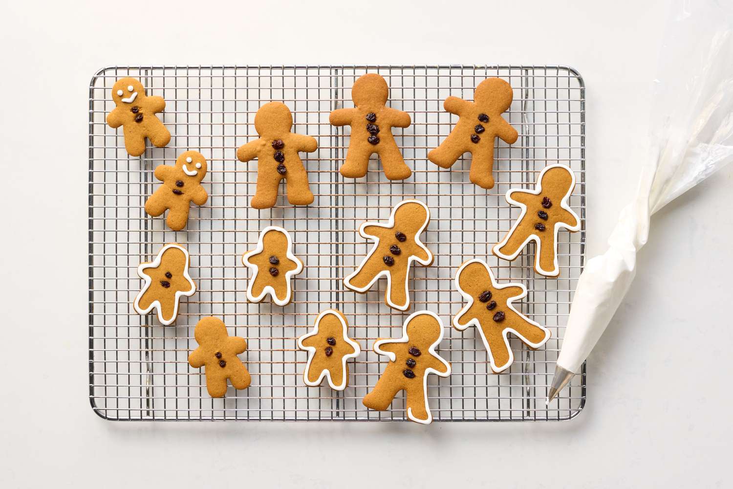 Gingerbread cookies on a cooling rack with a piping bag nearby some decorated with buttons