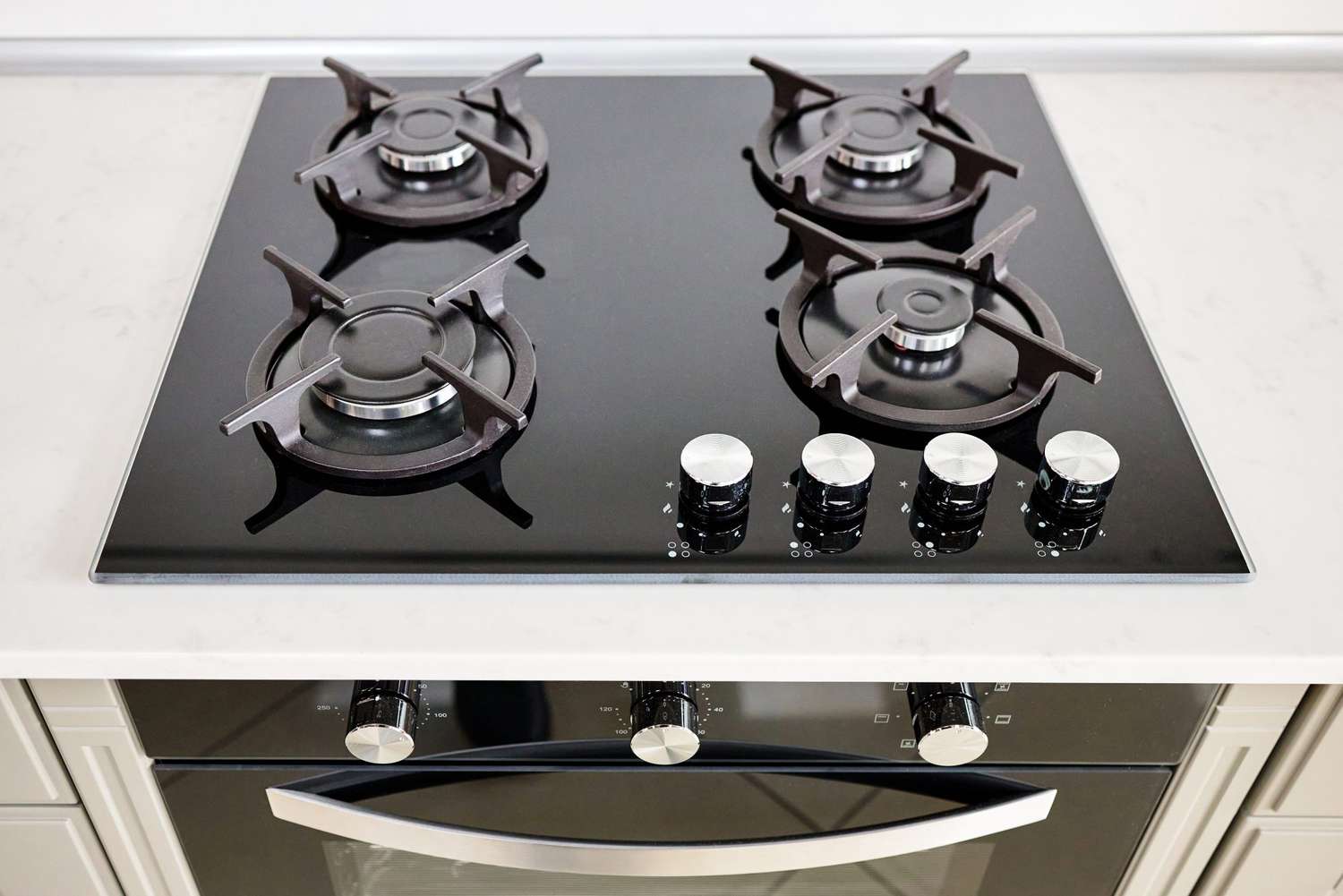 Modern built-in oven and gas stove classic design in dark tones under light stone marble or granite countertop in interior of contemporary kitchen.