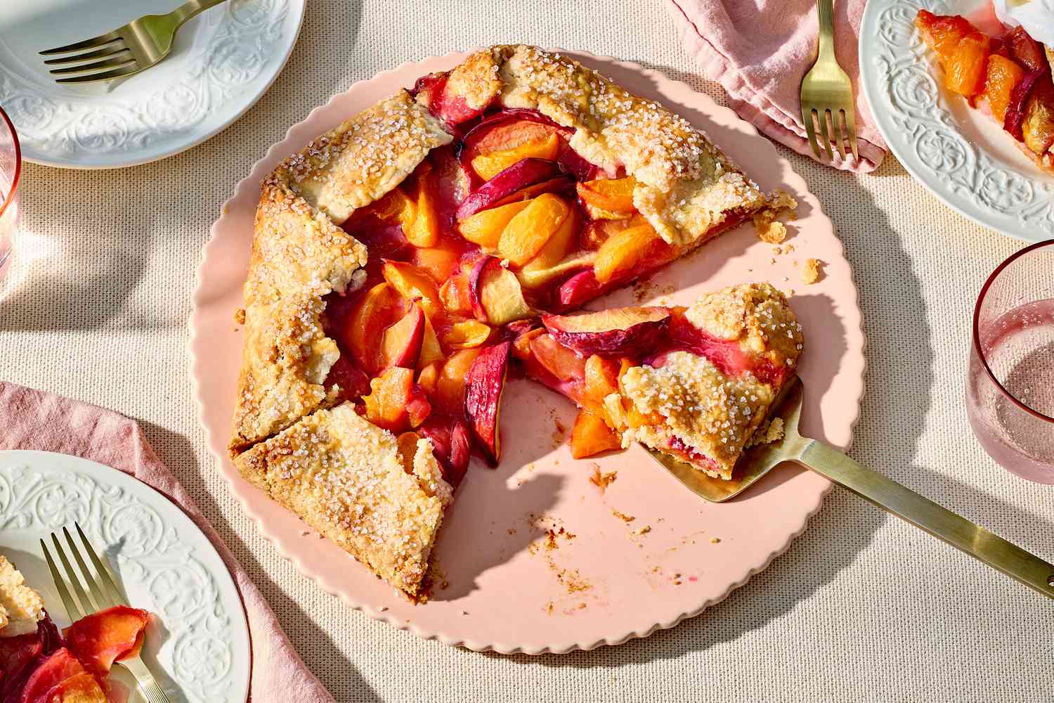 Stone fruit galette partially sliced, placed on a decorative plate with forks on the side
