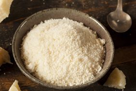 Bowl of grated cheese on a wooden surface with a spoon nearby