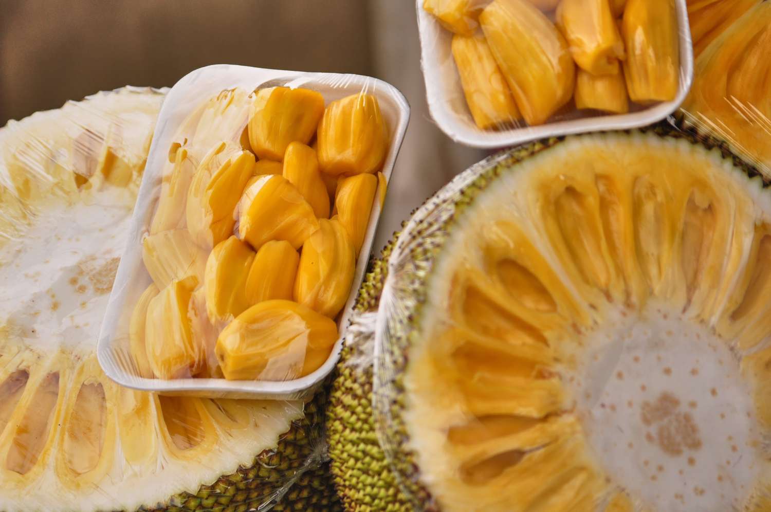 A half-cut fresh jackfruit and jackfruit meat are displayed in a plastic container and available for sale at the market.