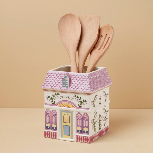 Ceramic utensil holder shaped like a house containing wooden kitchen tools