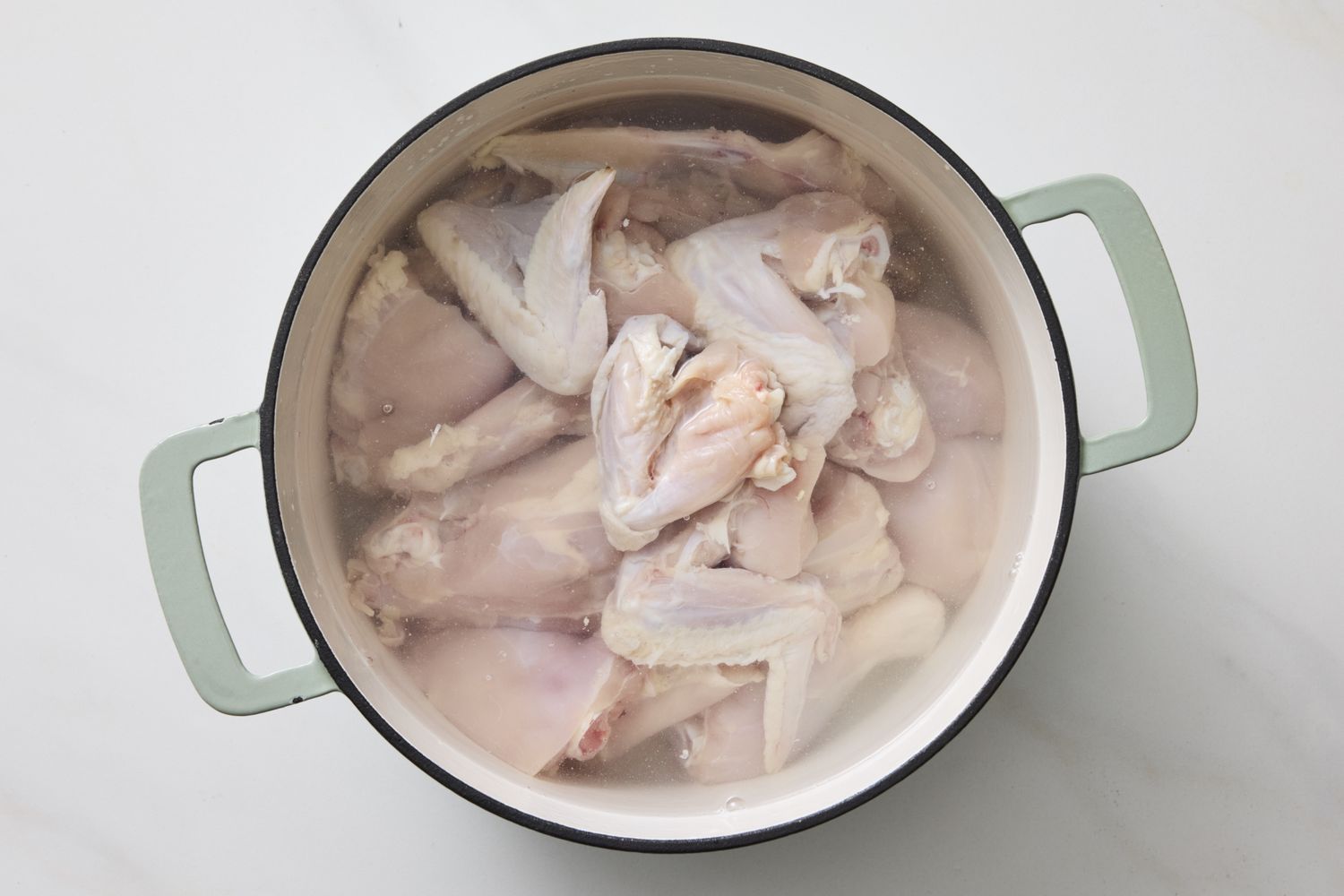 A cooking pot filled with raw chicken parts submerged in water likely being prepared as chicken stock