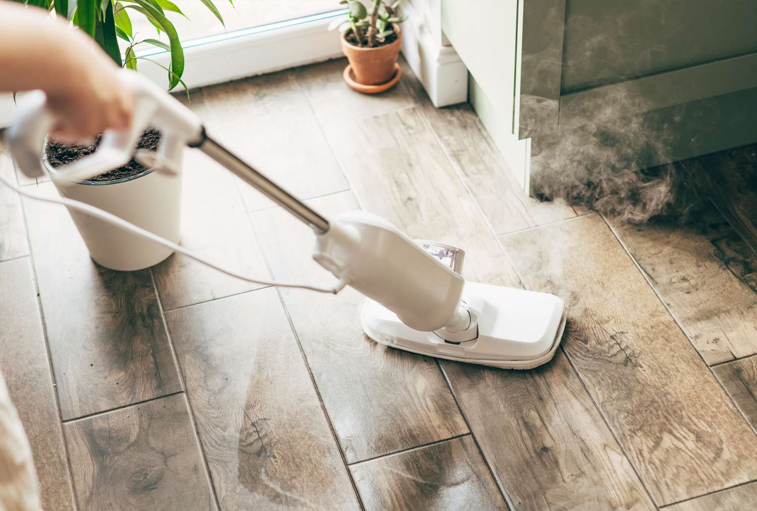 A steam mop being used on a wooden floor inside a home