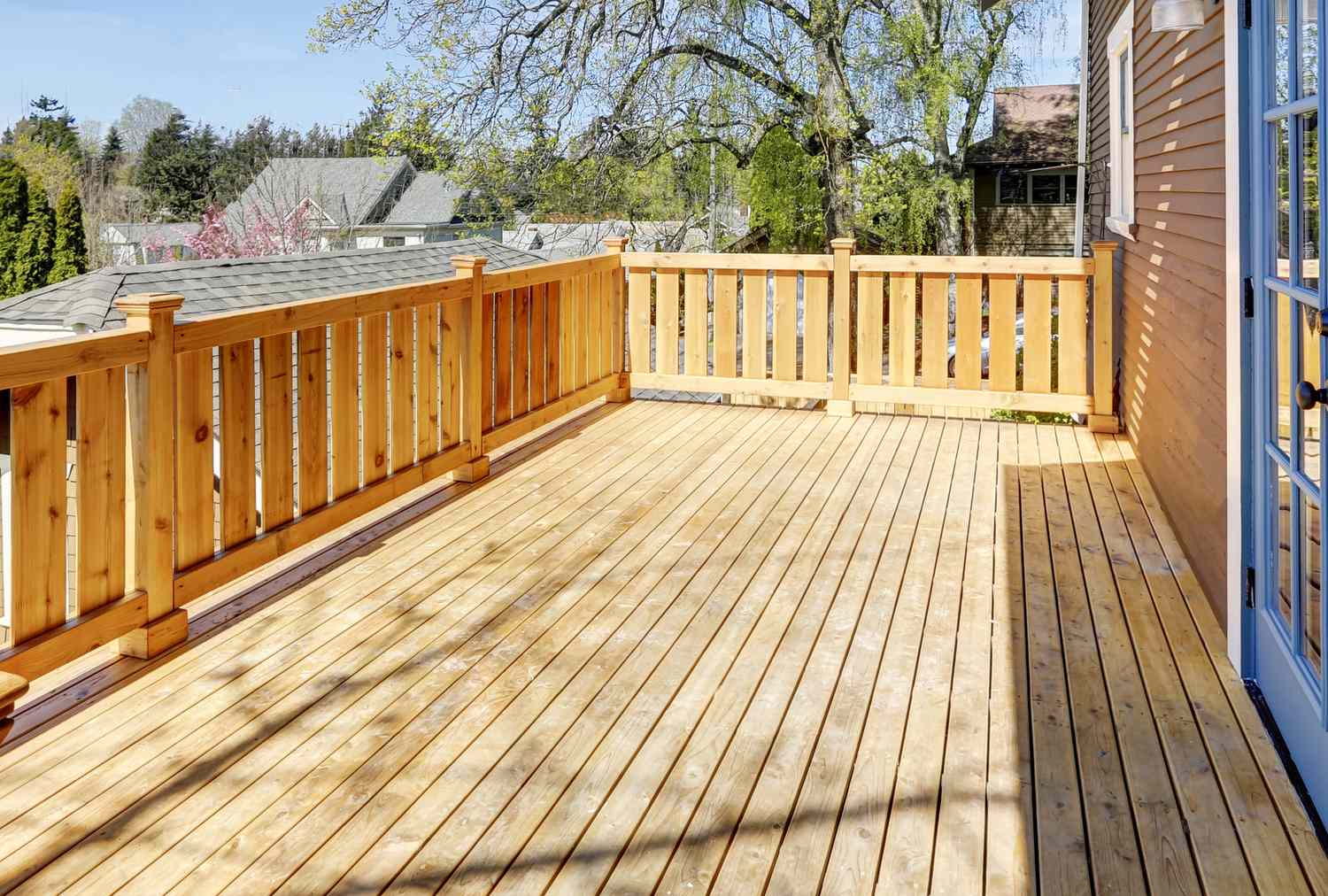 Wood deck attached to a house with a sturdy railing and view of trees and neighboring houses