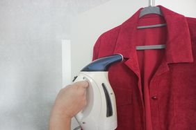 A handheld garment steamer in use on a red shirt hanging on a hanger