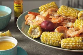 Platter of cooked shrimp corn on the cob and a red potato on a table with a sauce dish nearby