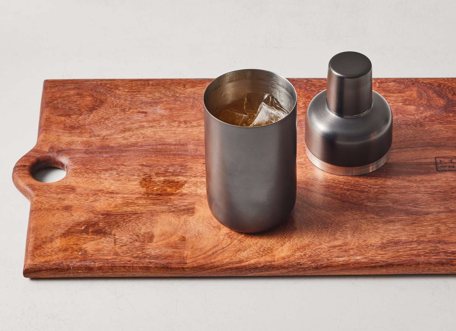 a metal cocktail shaker on wooden cutting board