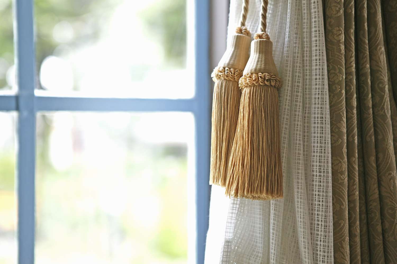 Curtain tassels hanging near a window with sheer and patterned curtains