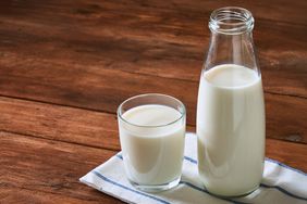A bottle and a glass of milk on a wooden surface with a cloth