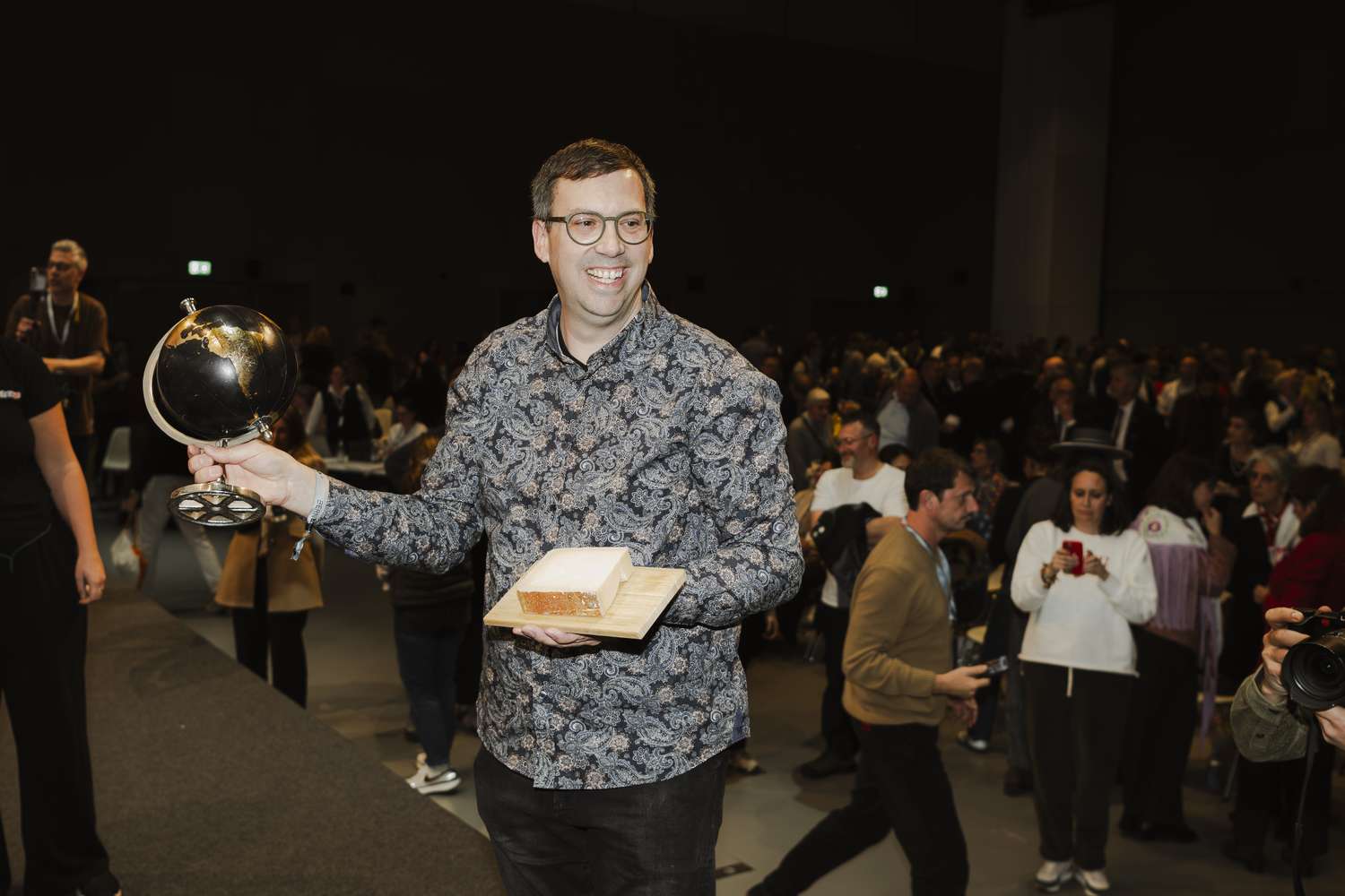 A person holding an award and a plaque in a crowded indoor setting smiling