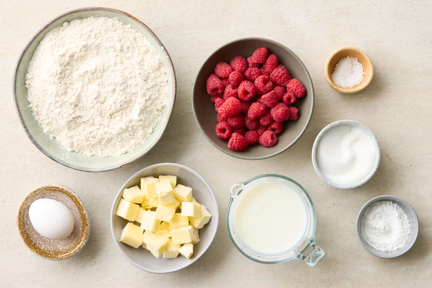 Ingredients for making raspberry scones including flour raspberries butter milk egg and other baking basics arranged on a countertop