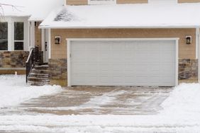 Snowcovered driveway and house exterior with a garage door